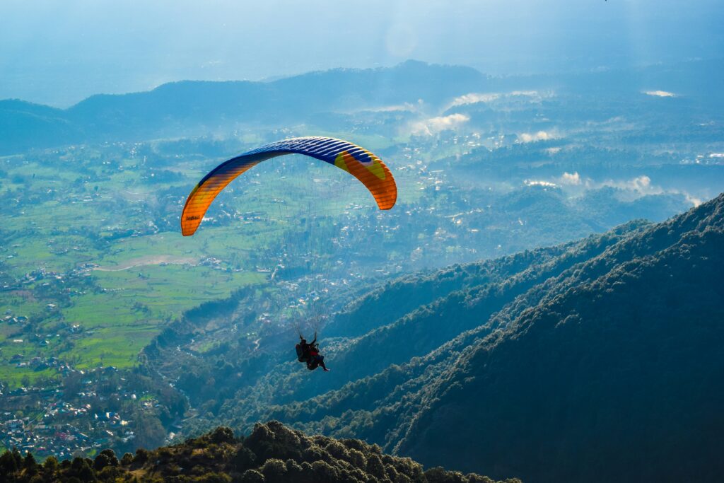 Paragliding Over Himalayas Adventure Sports Mountains Bir Billing Paragliding (A famous Indian site) High Altitude Flying Scenic Mountain Valley Orange Parachute Sky Himalayan Foothills View Extreme Sports Landscape Aerial View Village Paraglider Action Shot