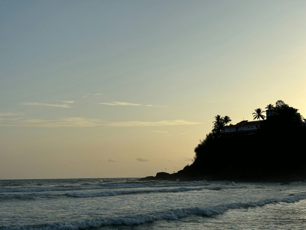 Coastal Cliff Sunset Beach Waves Dusk Tropical Silhouette Coast Ocean Horizon Sunset Hotel on Cliff Edge Palm Trees Silhouette Sea Waves Twilight Resort Coastal View Beach Landscape Evening Kovalam Beach India (Based on common features)
