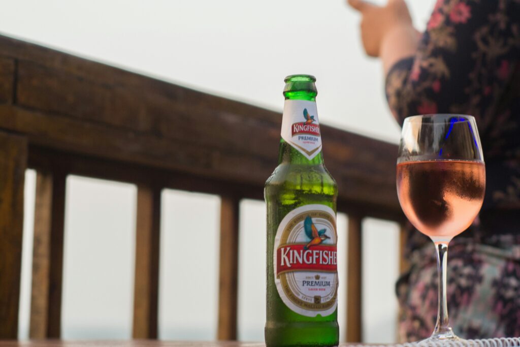 Kingfisher Premium Beer Beer Bottle Wine Glass Indian Lager Drink Alcohol Beverages Table Outdoor Bar Drinks Rose Wine Beer Relaxing Drinks Patio Goa Beer Scene (Implied context) Kingfisher Bottle Close-up Lager and Wine Pairing
