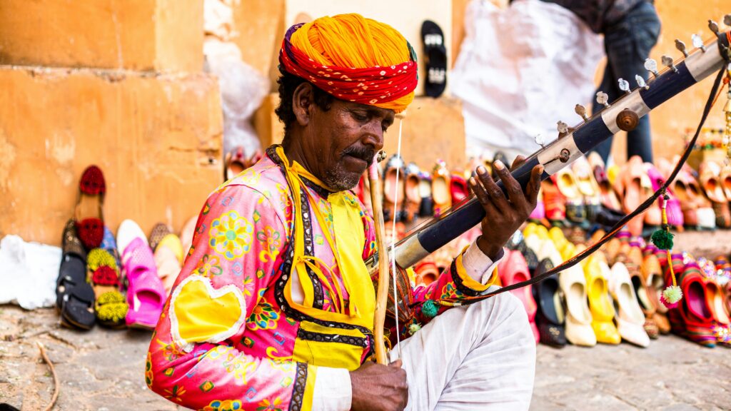 rajasthani folk musician traditional attire indian street performer playing string instrument man in colorful turban and kurta rajasthan traditional music india cultural portrait musician near jooti footwear display rajasthan culture vibrant colors street scene swastik arora indian travel photography amber fort jaipur street artist ragi or sarangi player traditional indian music indian folk music and handicraft market